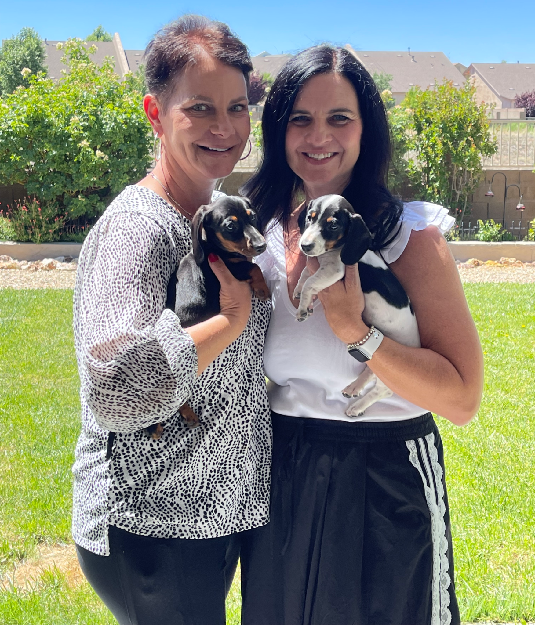 Woman outdoors with friend, holding puppies, smiling together after hair loss journey