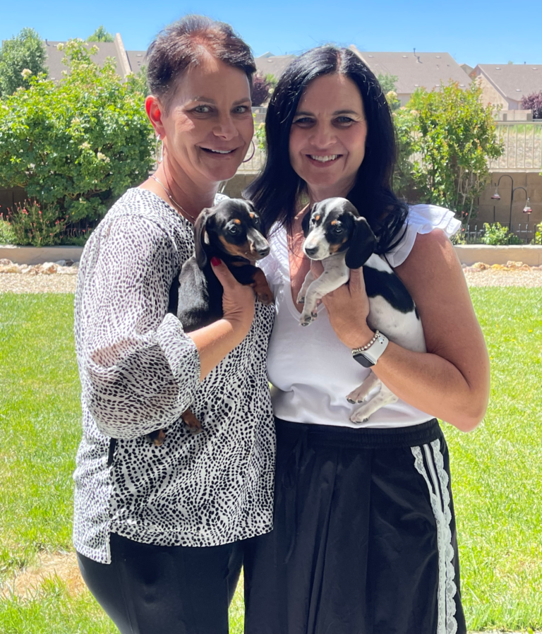 Woman outdoors with friend, holding puppies, smiling together after hair loss journey
